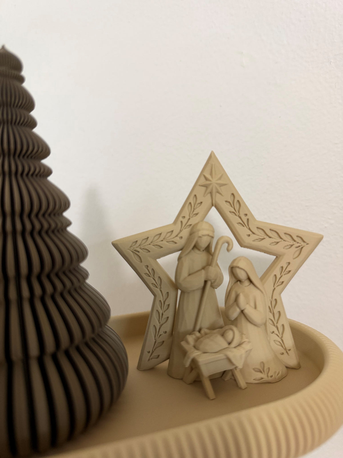 Primer plano del Nacimiento beige con María, José y el Niño Jesús dentro de una estrella decorada con hojas, acompañado de arbolito bronce y bandeja Japandi acanalada.